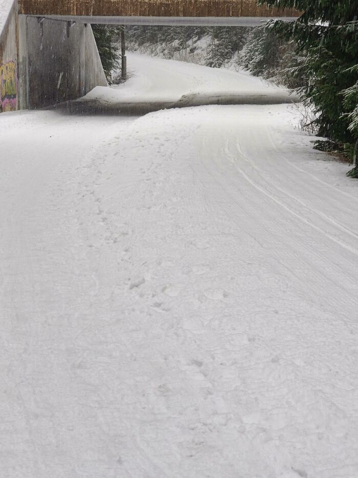 Snow-covered pathway under a bridge with footprints and ski tracks, showcasing small genius things some countries do.