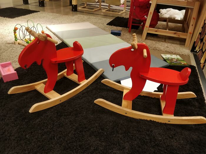 Two red wooden rocking moose toys on a black carpet in a children’s play area, showcasing small genius design ideas.