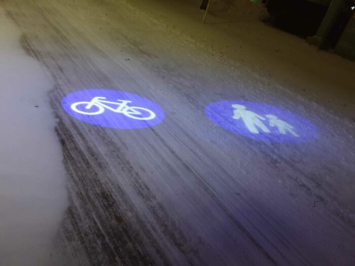 Bicycle and pedestrian lane symbols projected as blue lights on a snowy road showing small genius things some countries do.