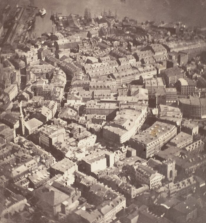 Aerial black and white 19th century photo showing historic city buildings and streets from above.