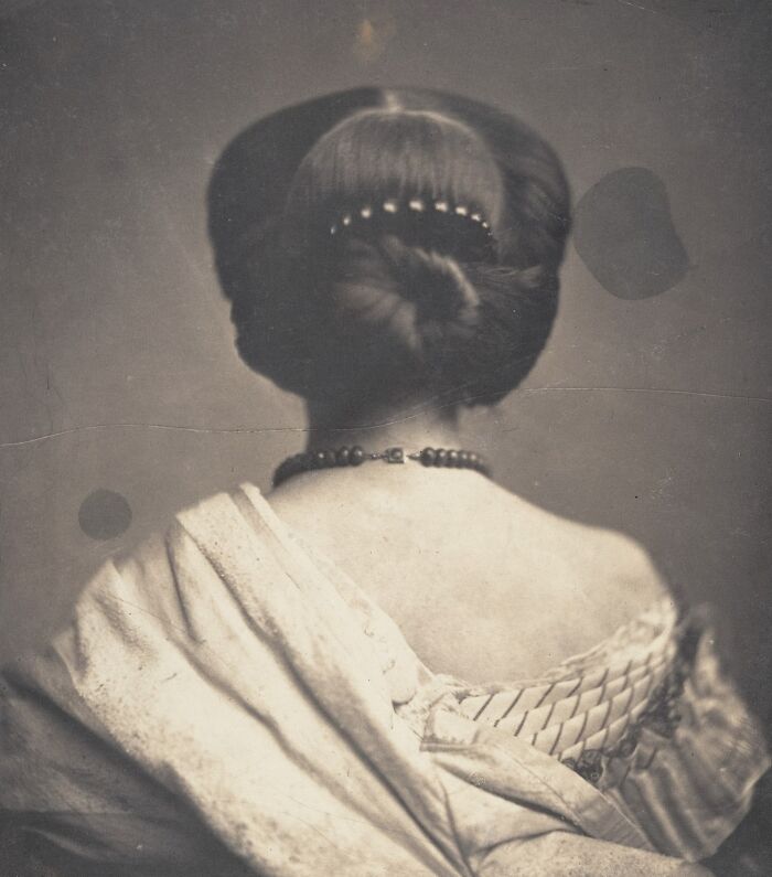 19th century photo showing a woman with an elegant updo hairstyle and a decorative necklace from behind.