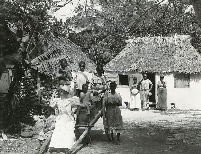 19th century invaluable photo showing a group of people in traditional attire outside thatched-roof houses.
