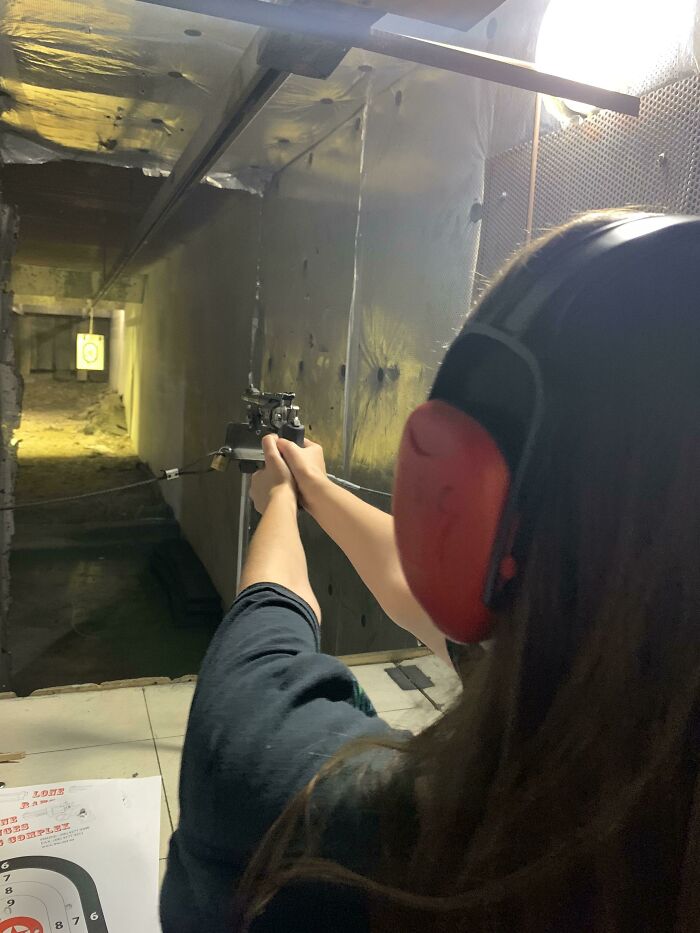 Person wearing ear protection aiming a gun at a target in an indoor shooting range, showcasing genius things some countries do.