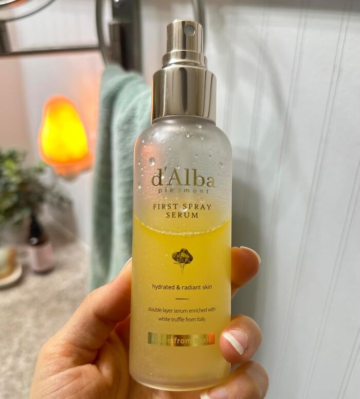 Hand holding a d'Alba first spray serum bottle, one of the most wished for items burning up Amazon this week.