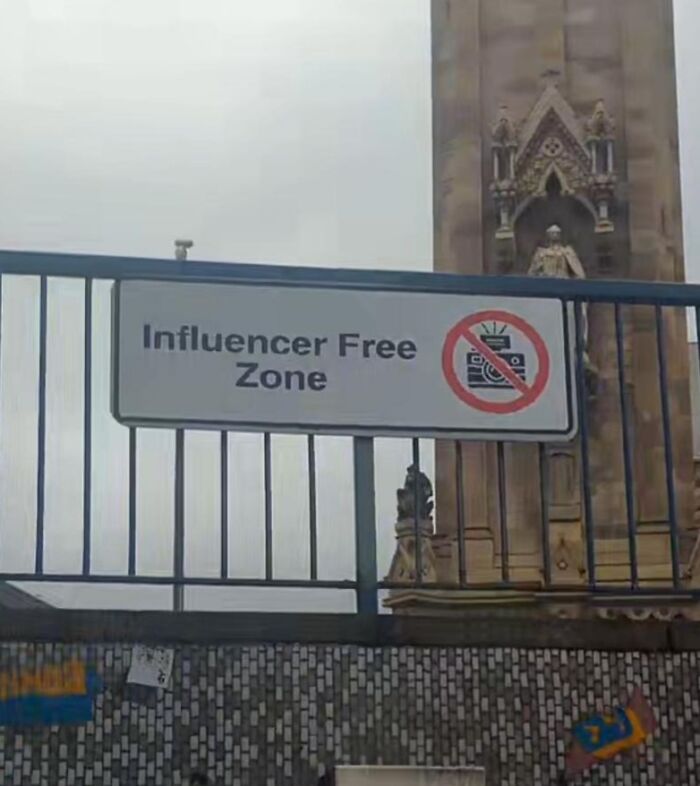 Sign reading influencer free zone on a fence in front of a historic building showing small genius things some countries do.