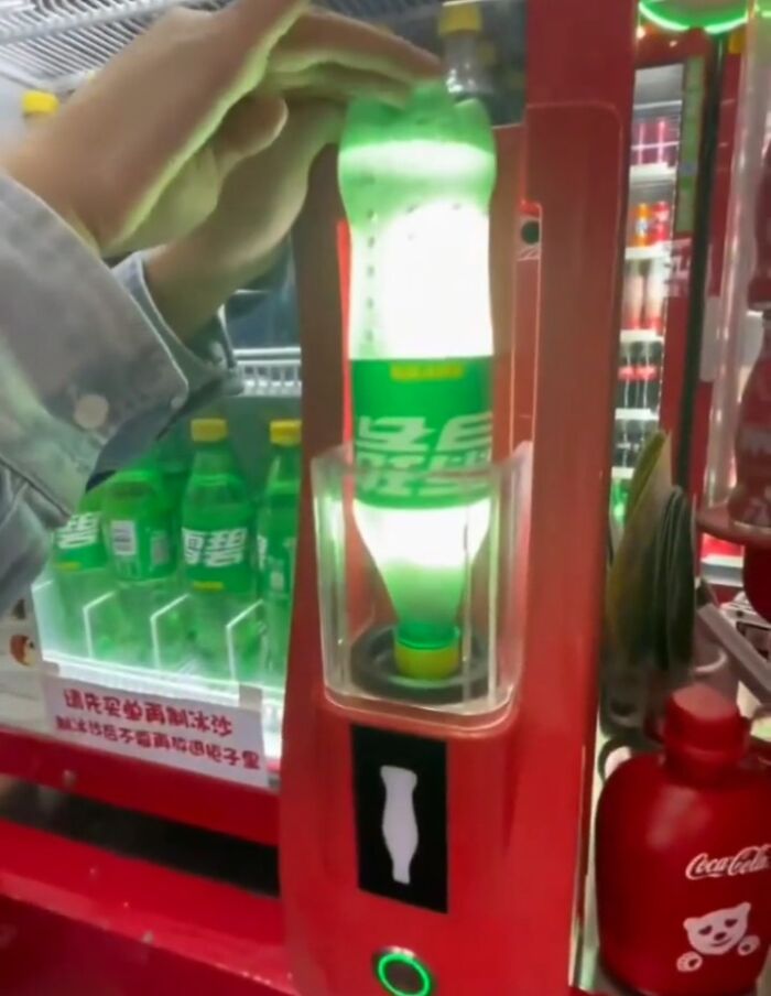 Hand inserting green soda bottle upside down into a red vending machine, showcasing small genius things some countries do.
