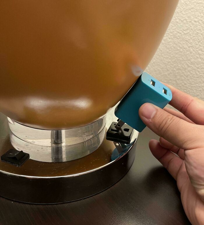 Hand plugging a charger into a lamp socket with the wrong adapter in a hotel room, an example of hotels messing up.