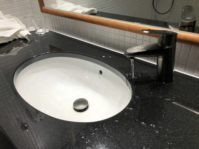 Leaking hotel bathroom faucet dripping onto black countertop, showcasing one of the many hotel mess-ups featured online.