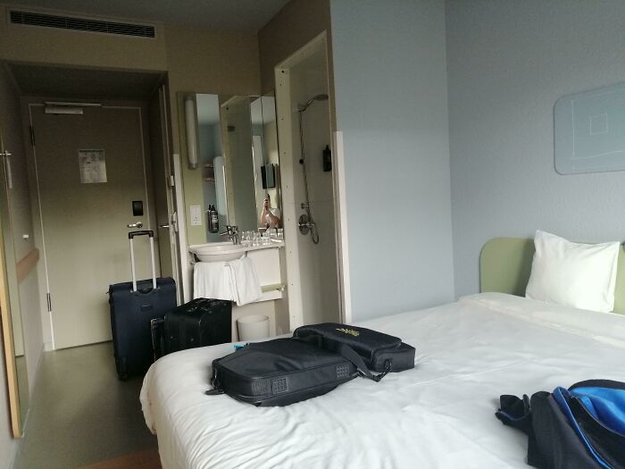 Small hotel room with an unmade bed, two suitcases by the door, and a cluttered sink, showing typical hotel mess-up issues.