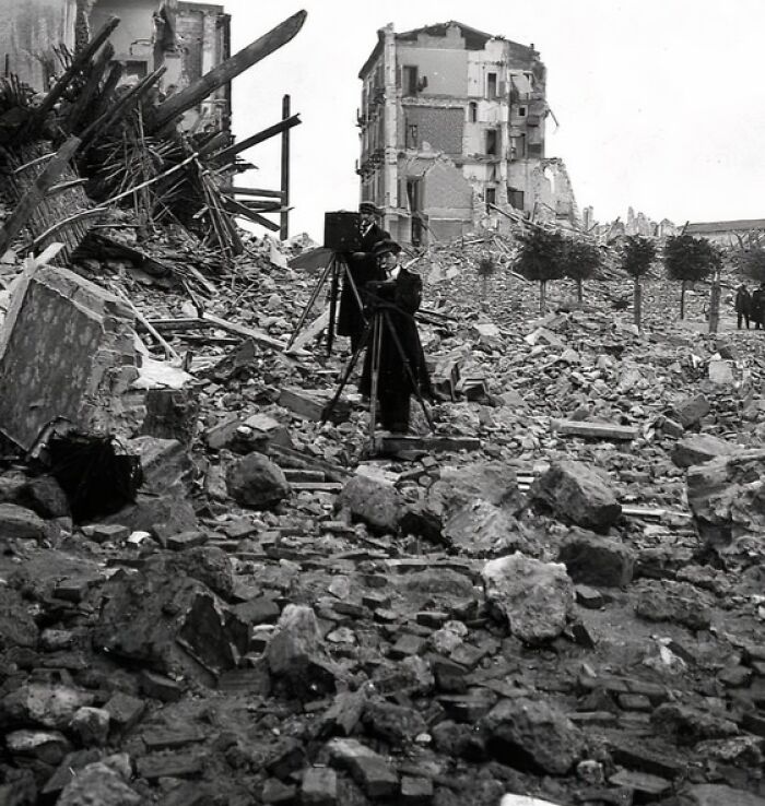 Photographers documenting the aftermath of a natural disaster amid large-scale rubble and destroyed buildings.