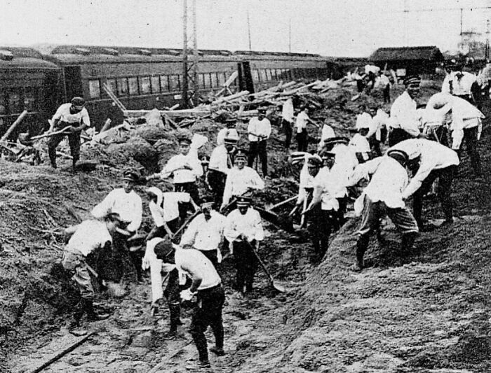 Group of workers digging and clearing debris near damaged trains after a large natural disaster in the last century.