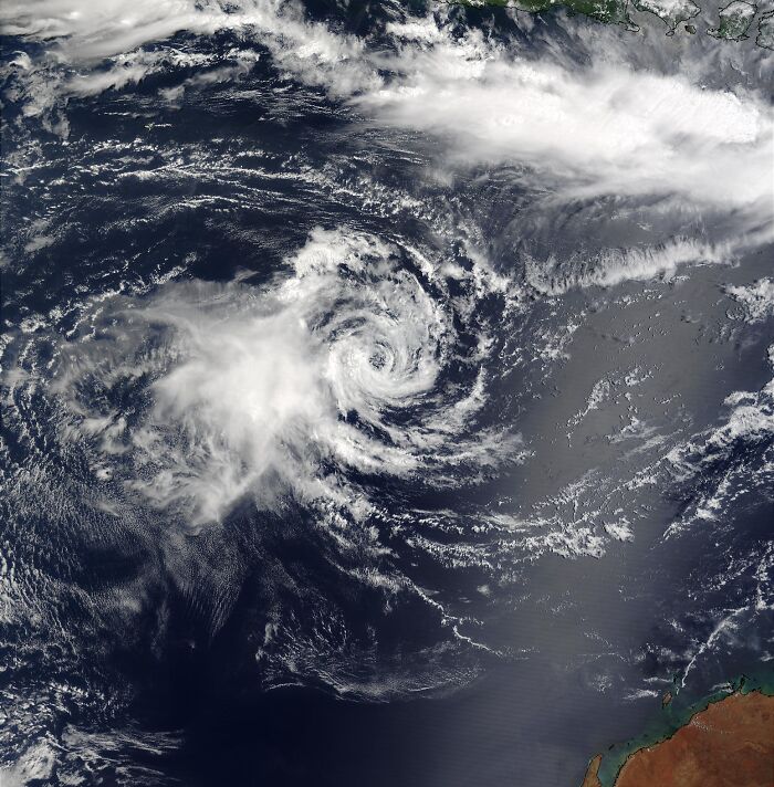 Satellite image of a massive natural disaster showing a large cyclone forming over the ocean with swirling clouds.