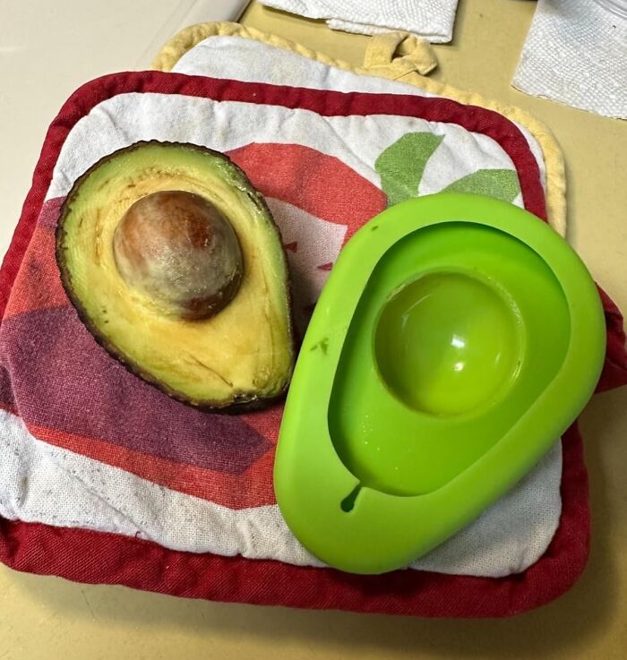 Green avocado slicer next to half an avocado on a colorful kitchen towel, showing a brilliant kitchen item for counter space.