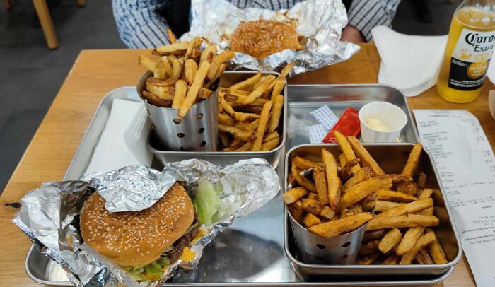 Two trays with burgers wrapped in foil and generous servings of fries, showcasing small but genius food presentation ideas.