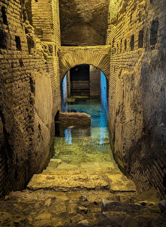 Ancient stone steps leading into clear water in a historic underground structure showcasing genius small country features.