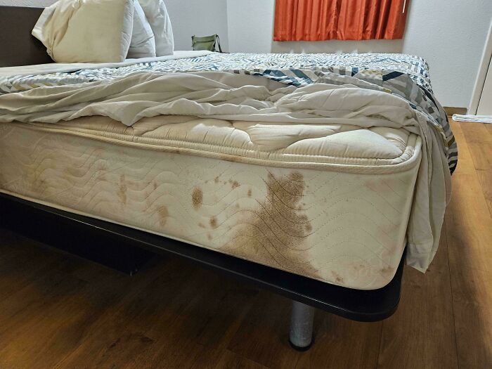 Stained mattress in hotel room with wrinkled sheets and pillows, showing a clear example of hotel mess-ups vented online.