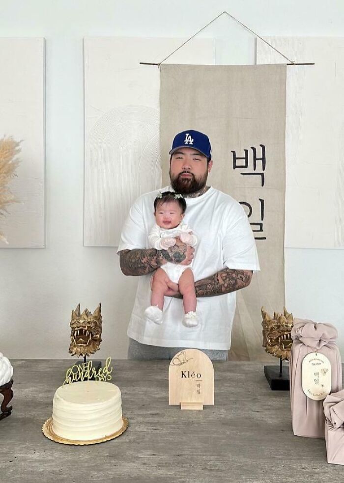 Padre con tatuajes sosteniendo a su bebé sonriente en una celebración familiar, mostrando momentos divertidos y tiernos de paternidad.
