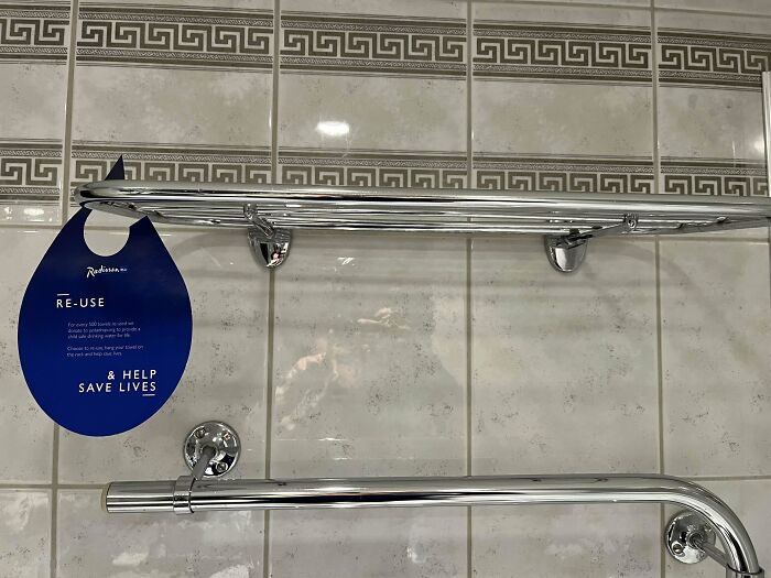 Hotel bathroom wall with chrome towel racks and a Re-use tag, showing a common hotels mess up from poor fixture placement.