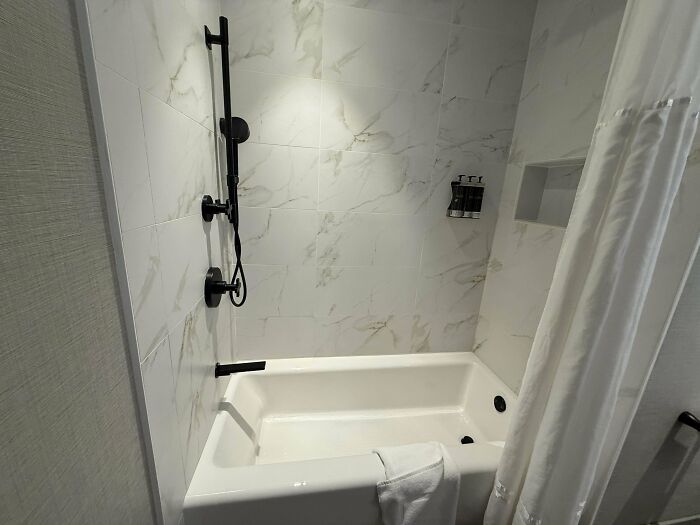 Hotel bathroom with black fixtures, white tub, and marble-patterned tiles, showcasing a hotel mess-up visible in the setup.