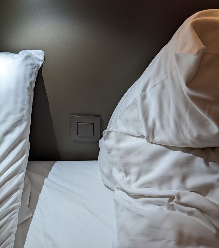 Hotel bedding mess up showing wrongly placed pillow and messy sheets near a wall switch, highlighting hotel fail moments.