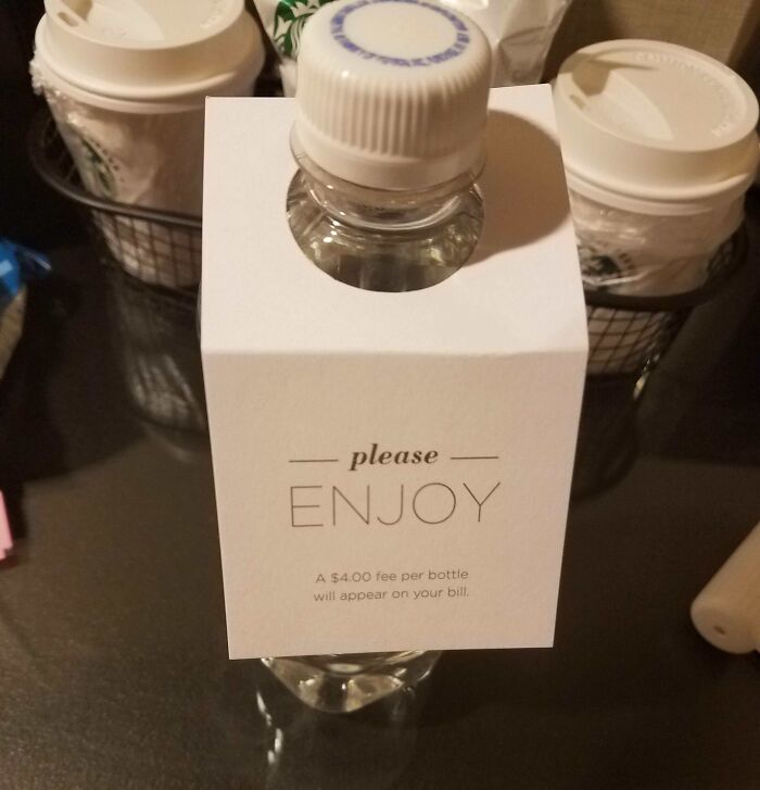 Clear plastic water bottle with a sign stating a $4 fee per bottle, highlighting hotels messed up fee issues online.