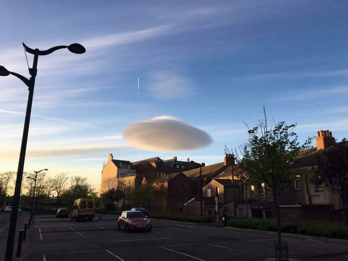 Unusual lenticular cloud formation hovering over residential buildings, a terrifying nature moment stopping people in their tracks.