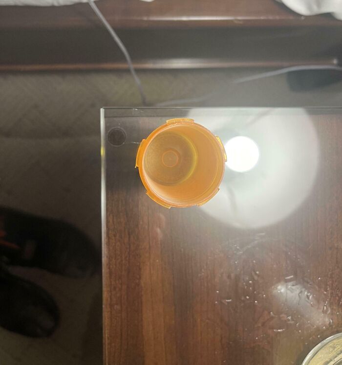 Top-down view of an empty pill bottle on a glass hotel table with visible water droplets and reflections.