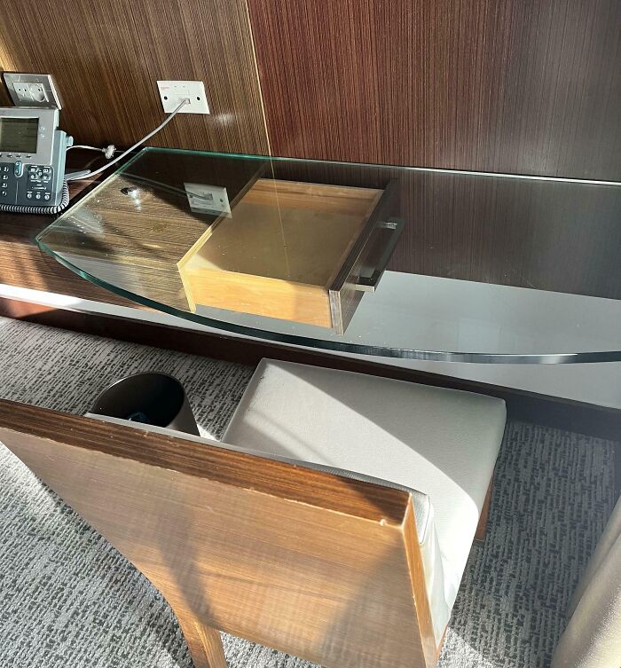 Glass hotel desk with a drawer preventing use and a chair tucked underneath in a hotel room setup.