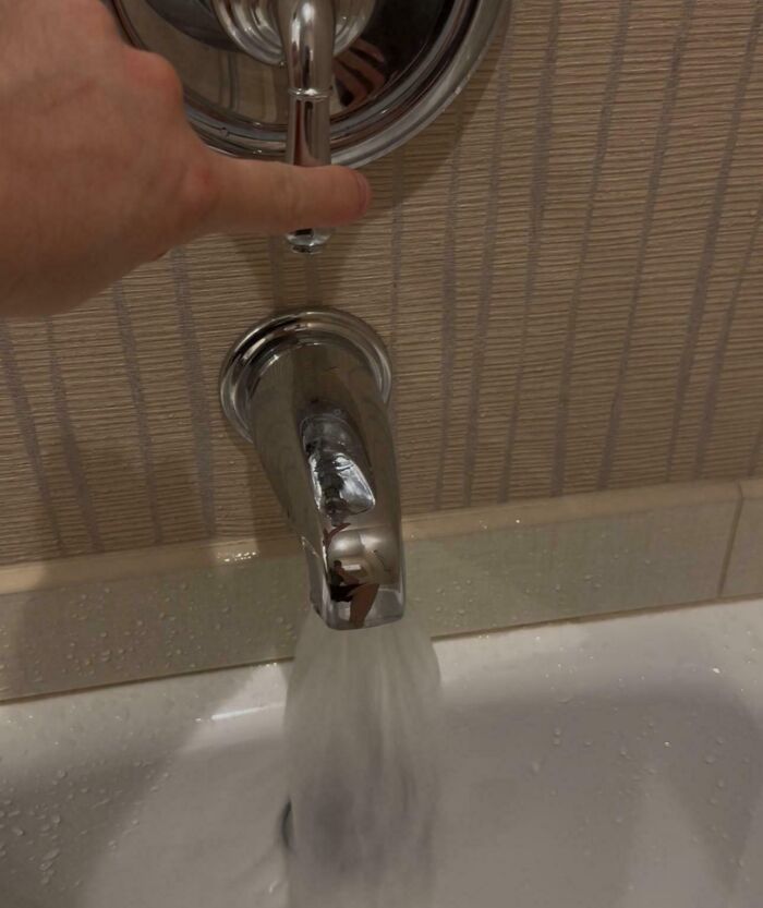 Hand turning hotel bathroom faucet with water flowing, showing a common hotel plumbing issue from guest experiences online.