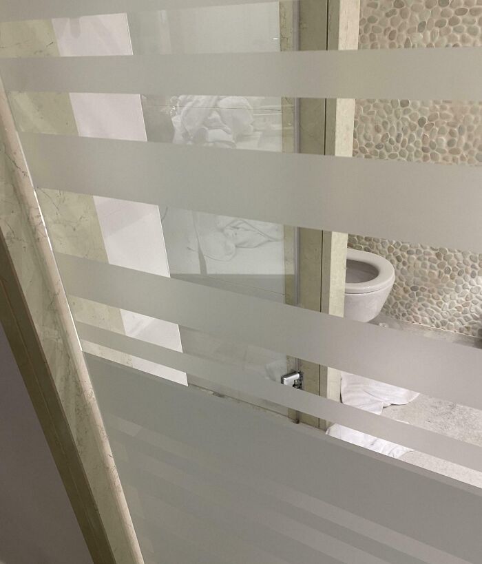 Frosted glass bathroom door in a hotel with poor privacy design showing toilet partially visible behind it.
