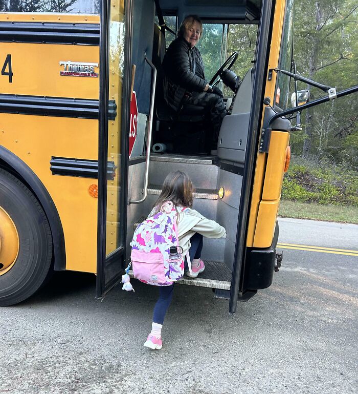 Dad smiling while helping daughter with backpack board a yellow school bus outdoors in a wholesome moment