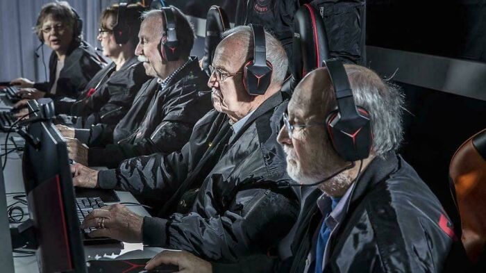 A group of elderly people wearing gaming headsets, focused on playing video games in a dark room.