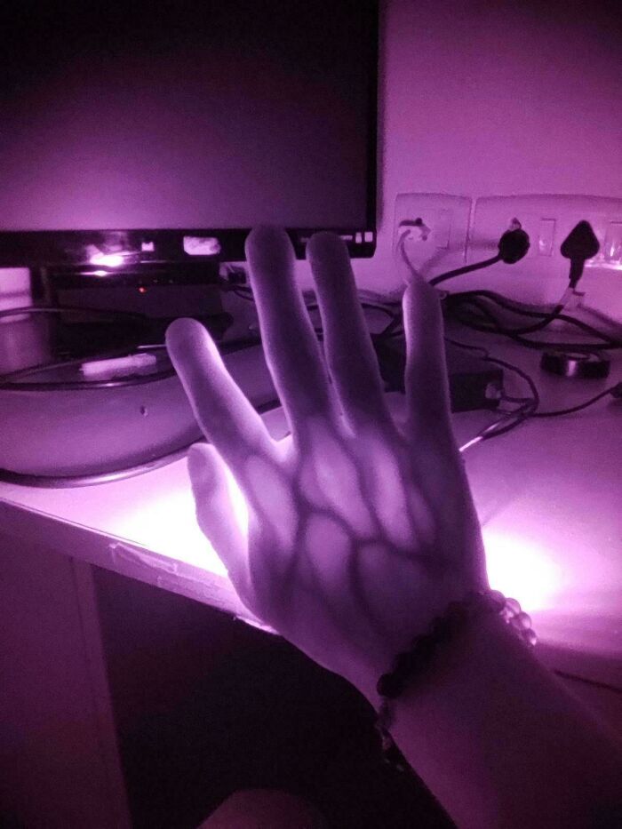Hand illuminated by purple light creating extraordinary and fascinating shadow patterns on a desk with electronic devices nearby.