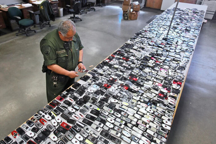 Man in uniform examining a large collection of old cell phones, showcasing extraordinary and fascinating things people saw.