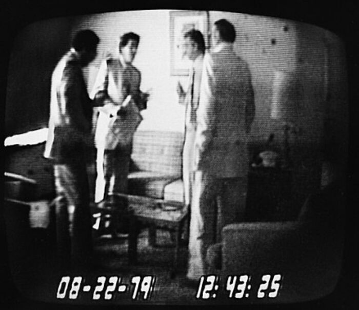 Black and white CCTV footage showing four men in suits indoors, capturing an extraordinary and fascinating moment.