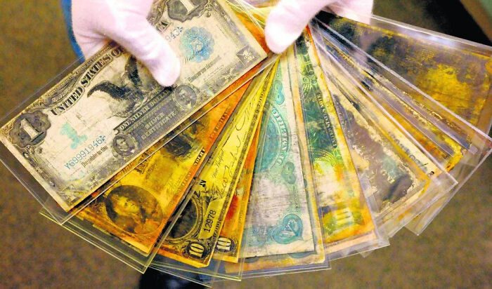Gloved hands holding a collection of extraordinary and fascinating old US dollar bills preserved in plastic sleeves.