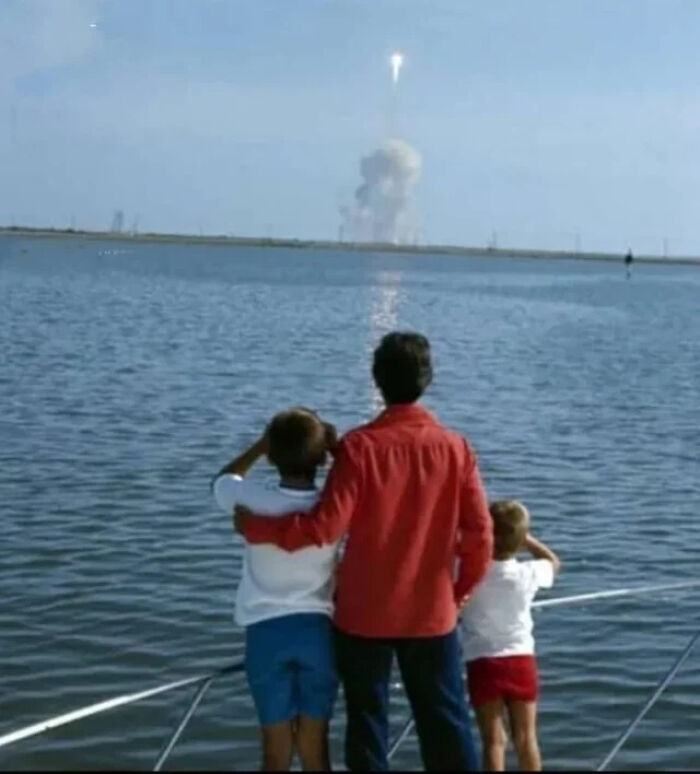 Three people on a boat watching a rocket launch over water, an extraordinary and fascinating sight to share.