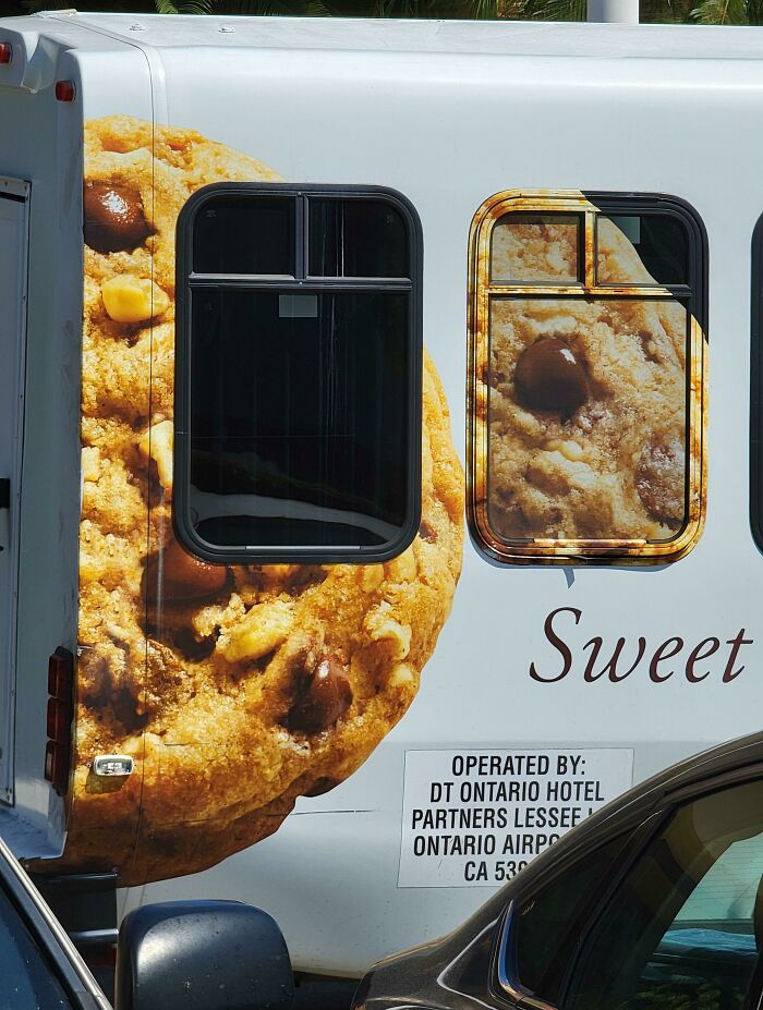 Large chocolate chip cookie printed on the side of a vehicle with windows interrupting the cookie image, showcasing funny advertising fails.