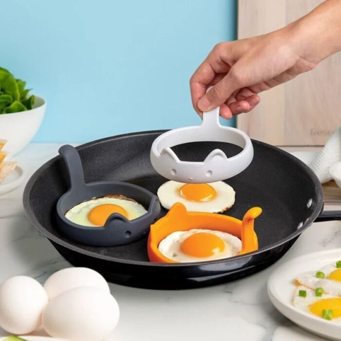 Hand using a cat-shaped silicone mold to cook eggs in a frying pan, showcasing weird kitchen inventions for easy cooking.