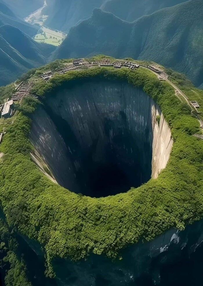 A extraordinary and fascinating massive circular sinkhole surrounded by greenery on a mountain ridge.