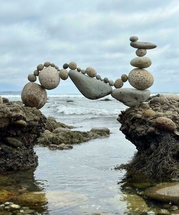 Intricately balanced stones forming an arch over a stream, showcasing extraordinary and fascinating natural art by the ocean.