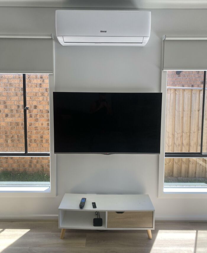 Minimalist living room with wall-mounted TV, air conditioner, and symmetrical windows highlighting imperfect alignment details.