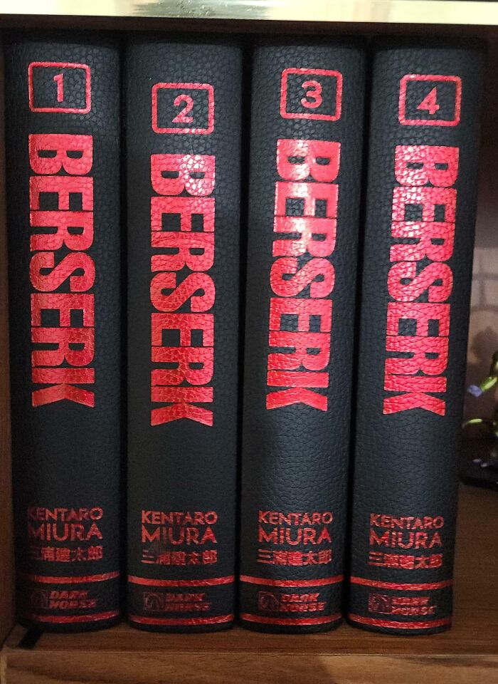 Four black and red hardcover Berserk manga volumes, neatly aligned on a wooden shelf.