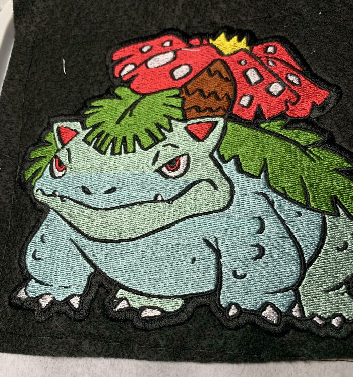 Embroidered patch of a fierce creature with leaves and a red flower on its back, highlighting imperfect things that annoy people.