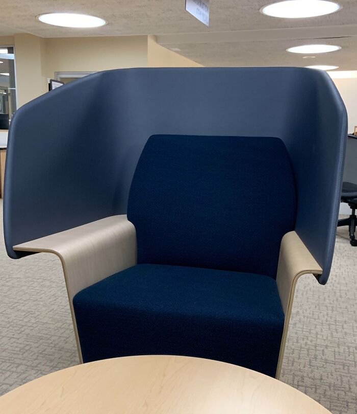 Modern blue privacy chair with curved high back and wooden armrests in office space, perfect for focus and concentration.