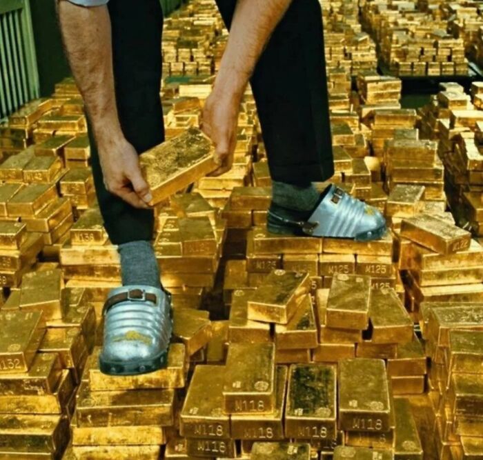 Person holding a gold bar while standing among stacks of gold bars, illustrating extraordinary and fascinating things seen.