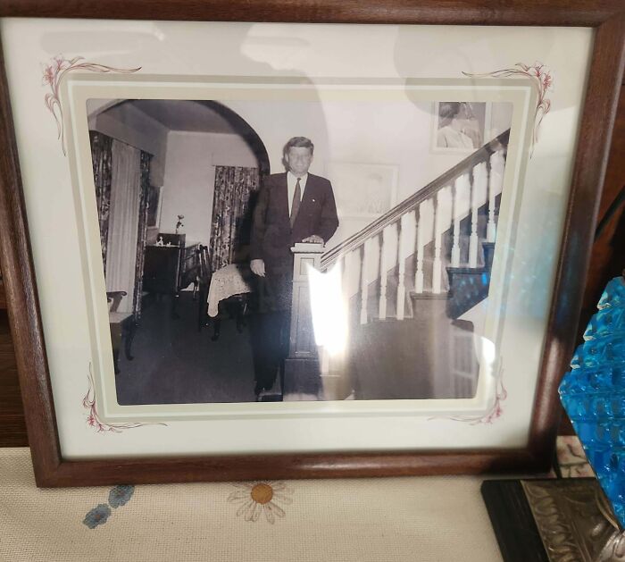 Black and white vintage photo of a man standing by a staircase in a framed picture on a table, extraordinary sight.