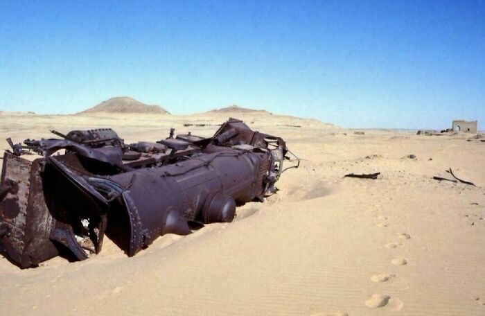 Rusty old steam locomotive wreck partially buried in desert sand, an extraordinary and fascinating sight.