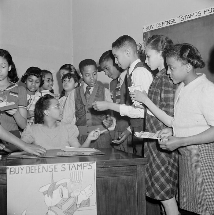 Students in a school during World War II gather to buy defense stamps as part of the wartime school efforts and activities.