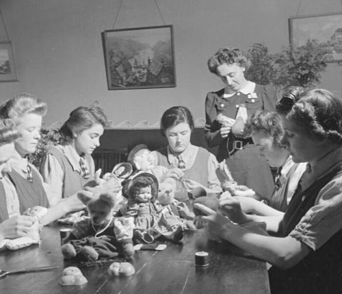 Women sewing dolls in a school classroom during World War II, showcasing daily life in schools worldwide during the war.
